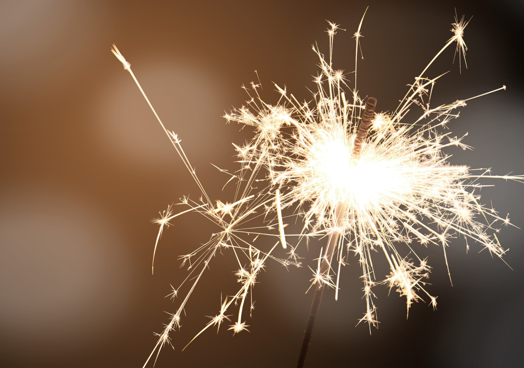 Brennende Wunderkerze mit funkelnden Lichtstrahlen vor dunklem, unscharfem Hintergrund
