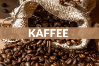Kaffeebohnen, teils verschüttet, liegen aus einem geöffneten Jutesäckchen auf Holztisch.