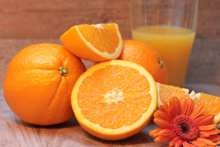Frische, ganze und aufgeschnittene Orangen mit einem Glas Orangensaft
