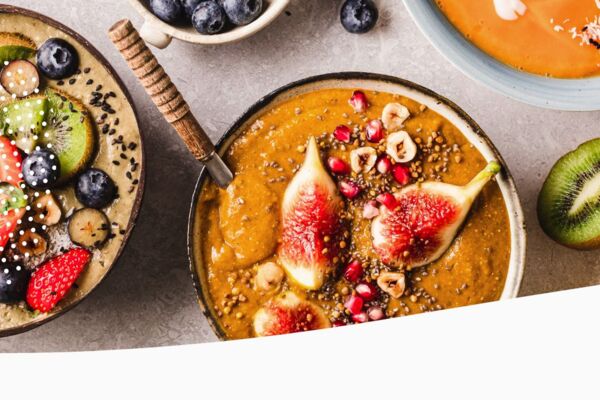 Bunte Frühstücksschalen mit frischen Früchten wie Kiwi, Erdbeeren, Blaubeeren und Feigen, garniert mit Samen und Nüssen.