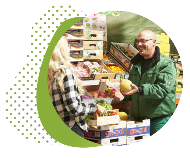 Mitarbeiter von Frucht Hartmann berät Kundin am Obst- und Gemüsestand im Privatverkauf.