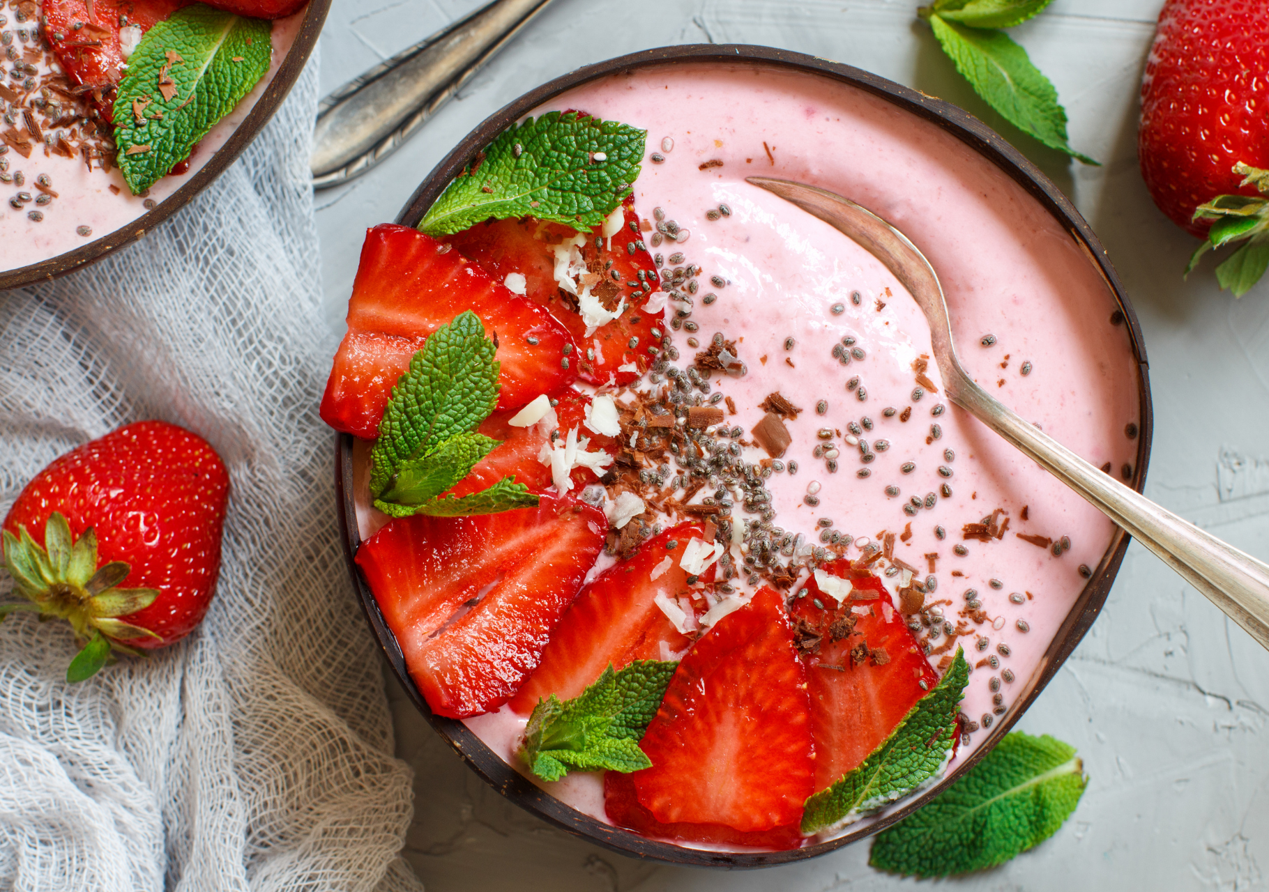 Erdbeer-Smoothie-Bowl garniert mit frischen Erdbeerscheiben, Minzblättern, Chiasamen und Schokoraspeln in einer Schale.